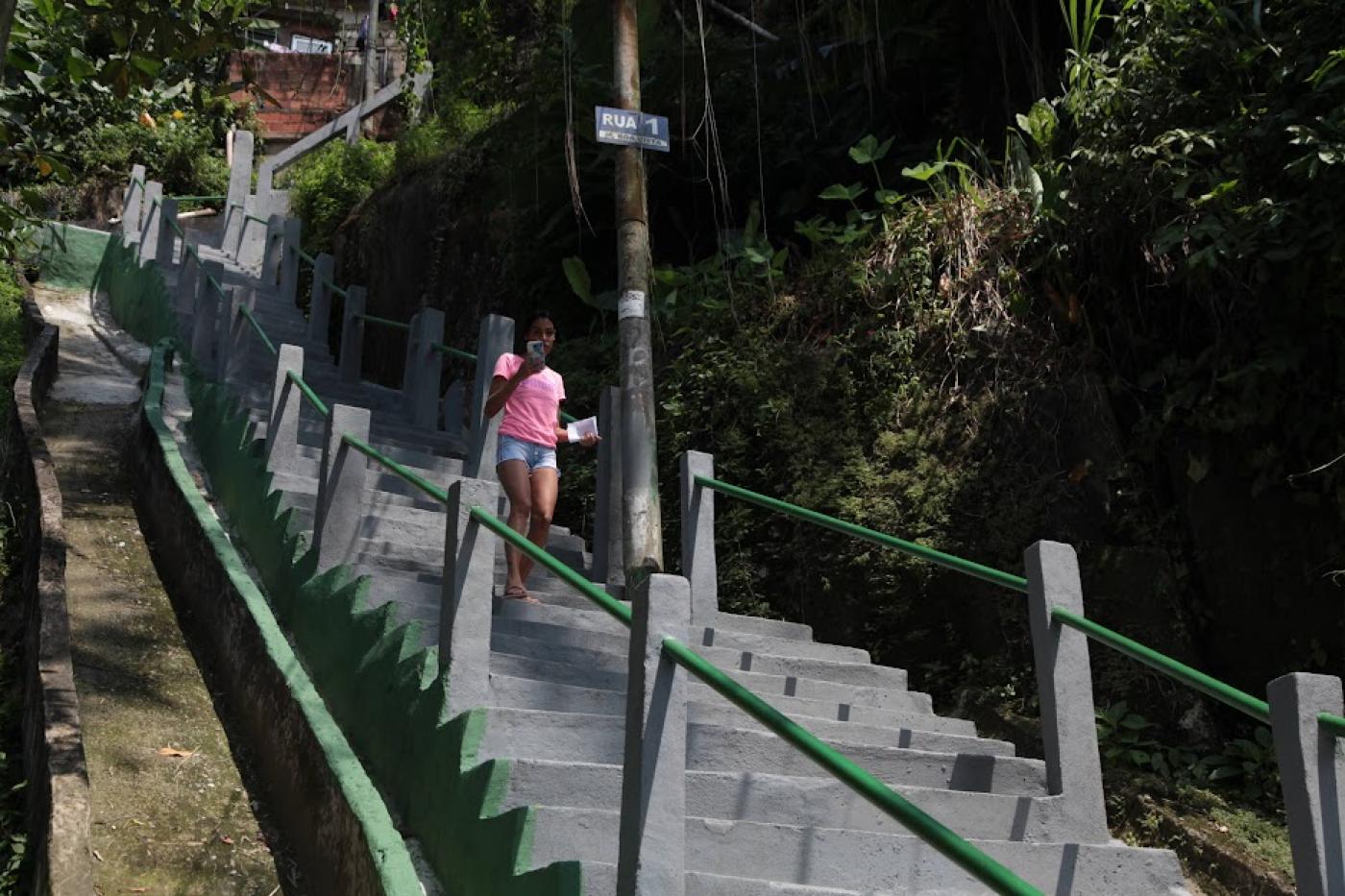 mulher está descendo escadaria no morro. Há vegetação do lado direito da foto. #paratodosverem 