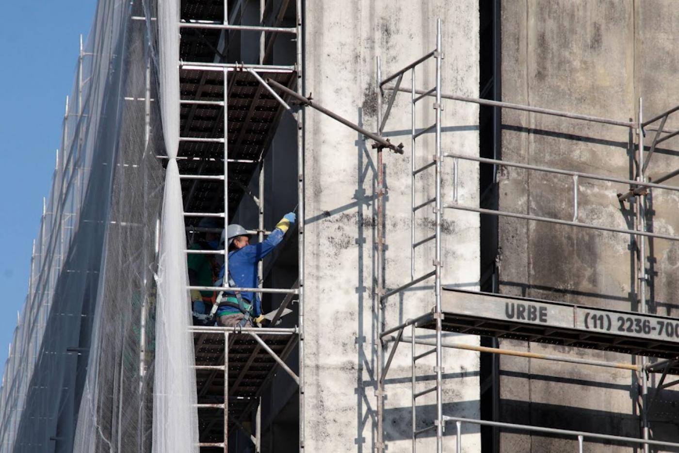 homem está em andaime reparando fachada de prédio. #paratodosverem 