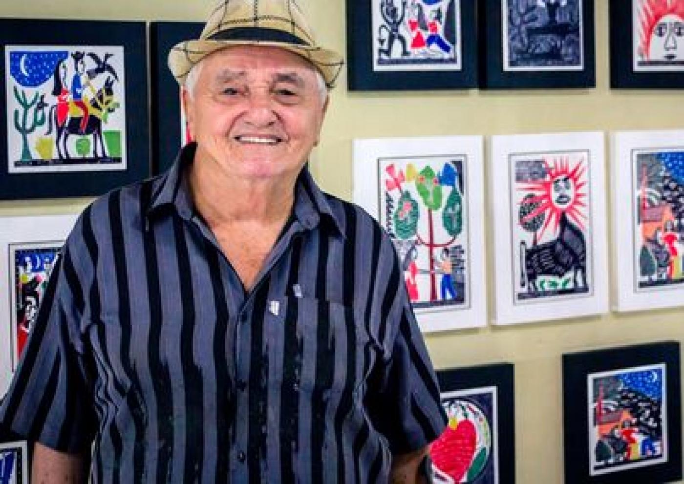 O artista J.Borges posa para foto com ilustrações própras ao fundo