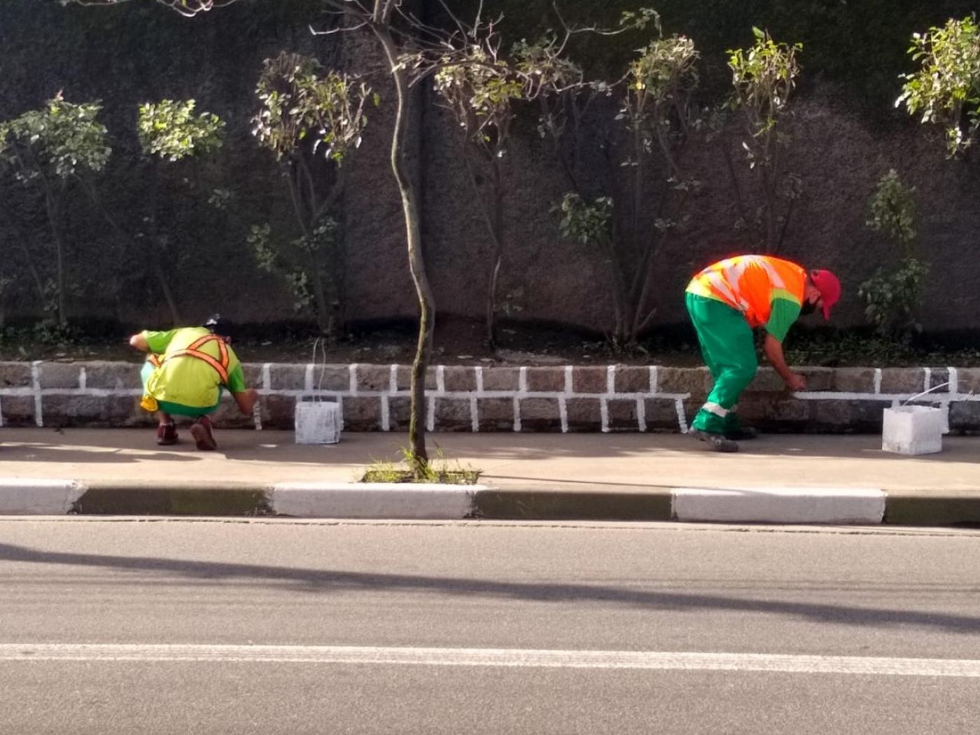 dois homens pintam jardineira junto a calçada. #paratodosverem