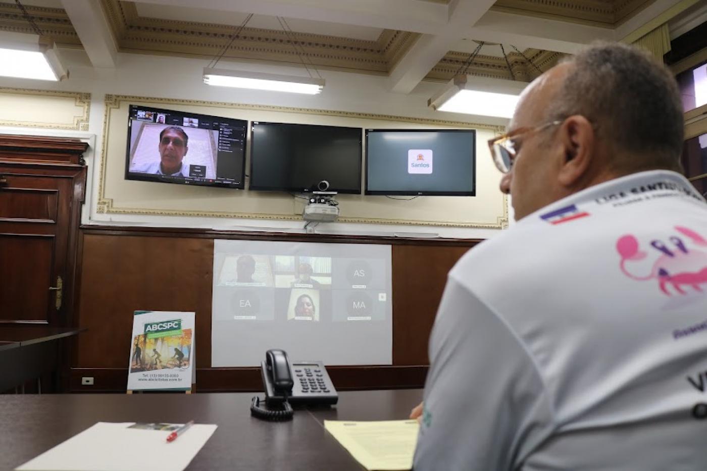 homem está de costas para a foto e de frente para telões. #paratodosverem