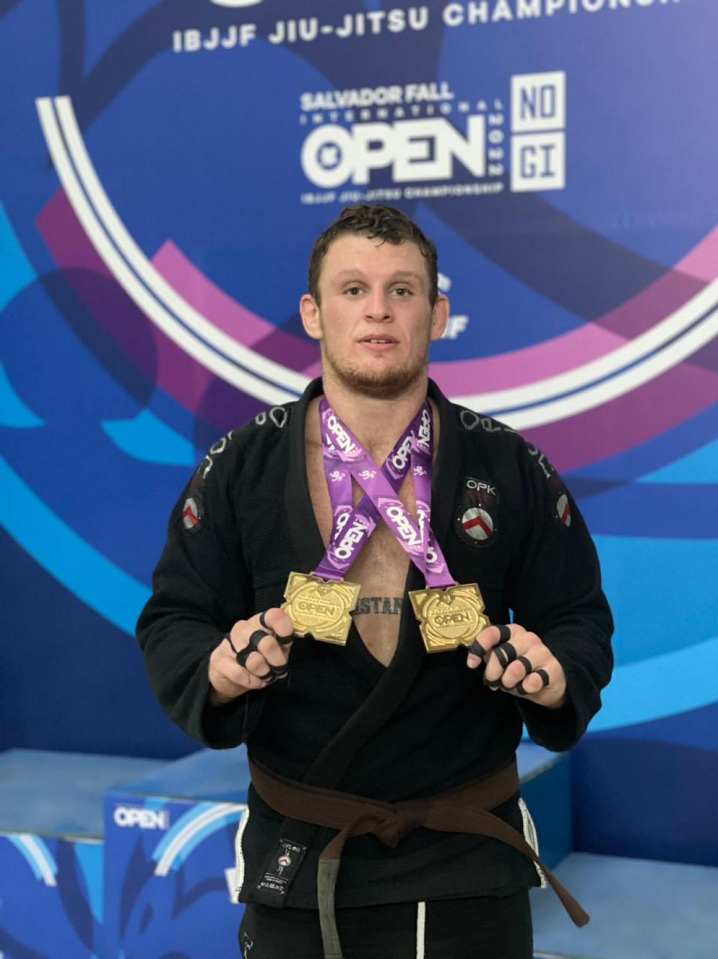 Christiano Tayfour Troisi segura com as mãos as medalhas penduradas no peito. #paratodosverem