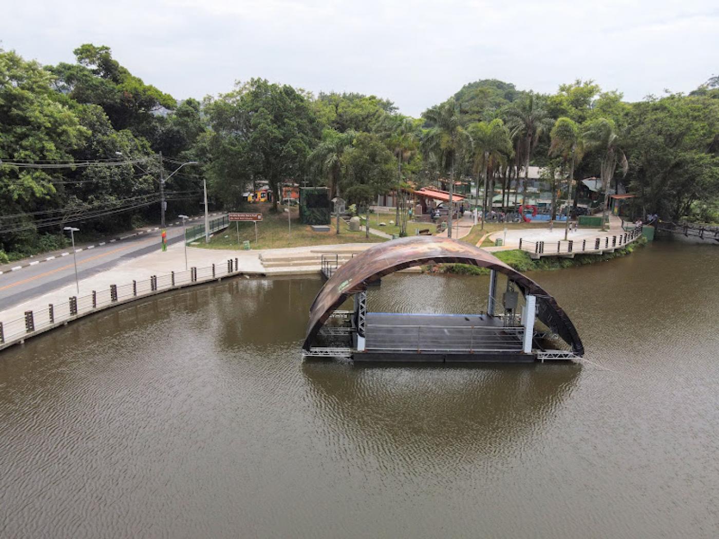 vista aérea da lagoa da saudade, com palco flutuante na água, vegetação e área de lazer ao fundo. #paratodosverem