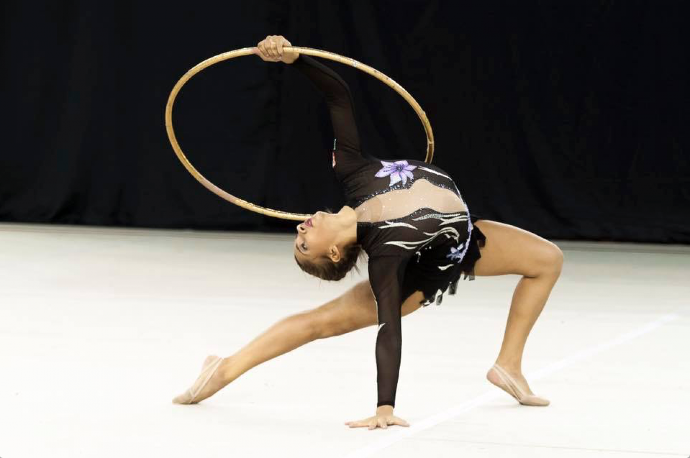 Menina está fazendo exercício em solo com arco. #Pracegover