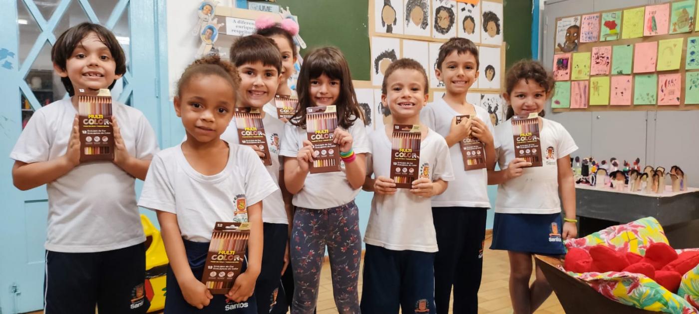 crianças posam para foto segurando caixas de lápis de cor. #paratodosverem 