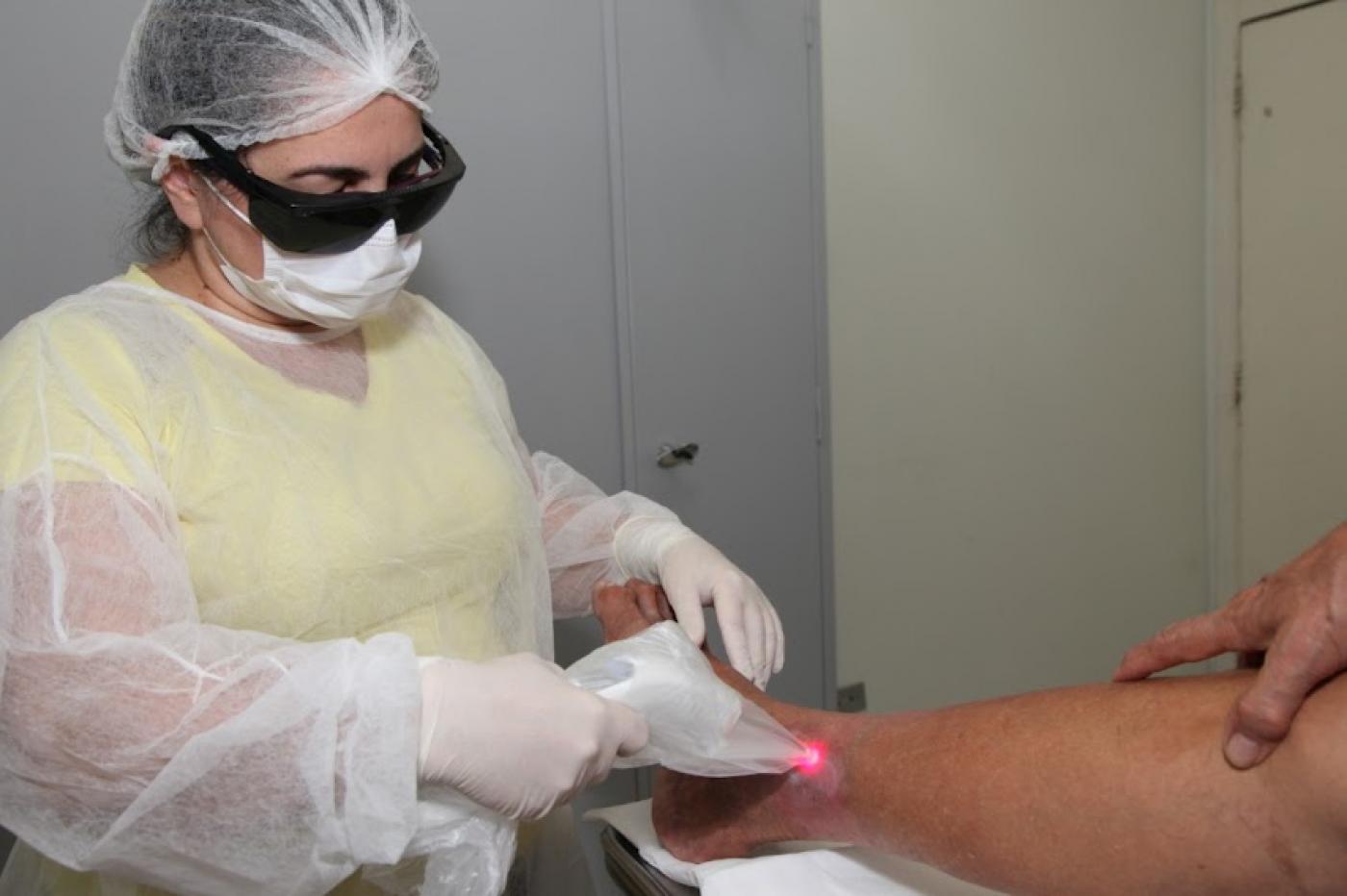 Enfermeira realiza aplicação de laser em pé de paciente. #paratodosverem 