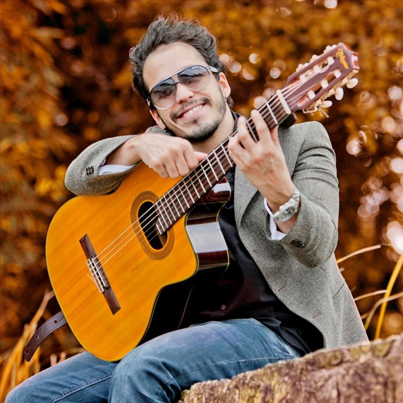 leandro ramajo posa para foto sentado segurando violão. #paratodosverem 