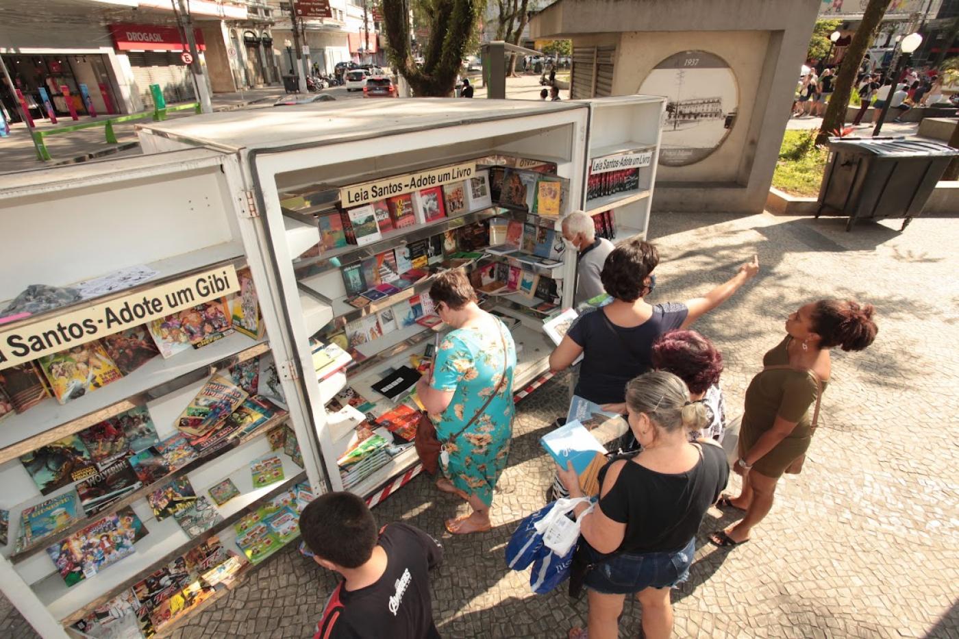 pessoas olhando o estande com livros #paratodosverem 