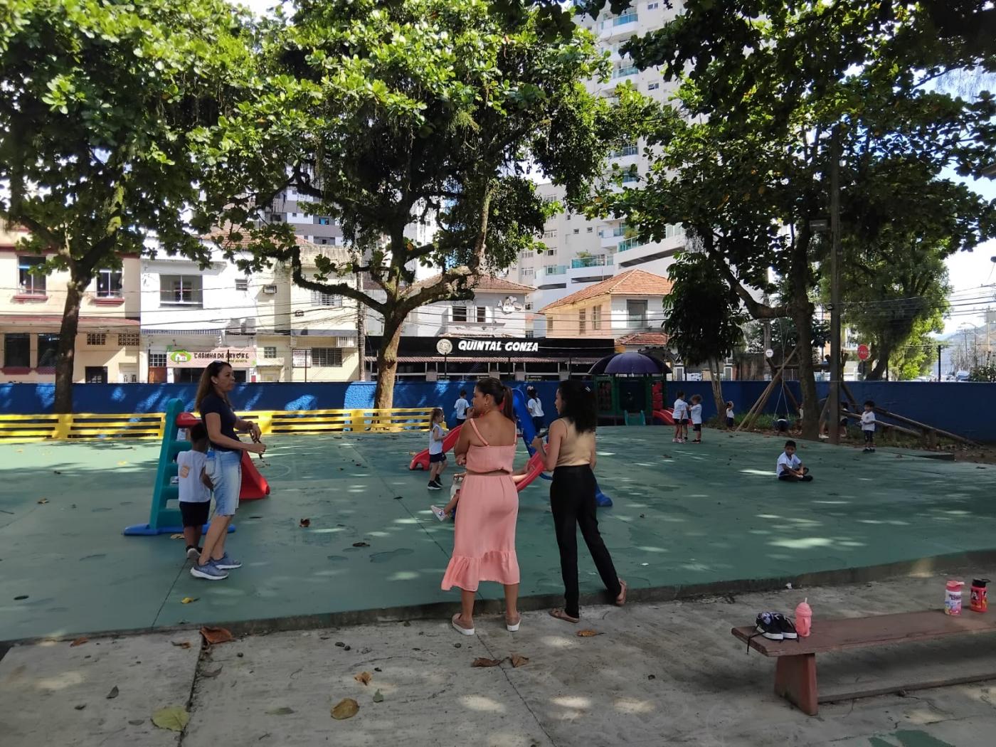pessoas estão em parque infantil com piso recém-pintado de verde. #paratodosverem