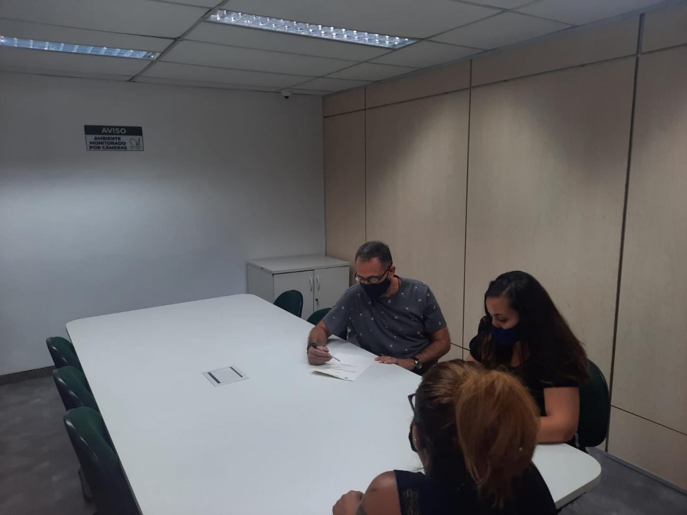Um homem e duas mulheres conferem documentação em sala de reunião. #pratodosverem