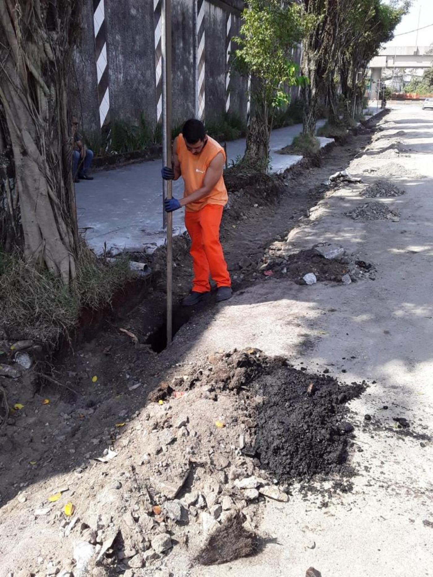 operário usa grande vara para introduzir em boca de lobo e limpar o fundo. #paratodosverem