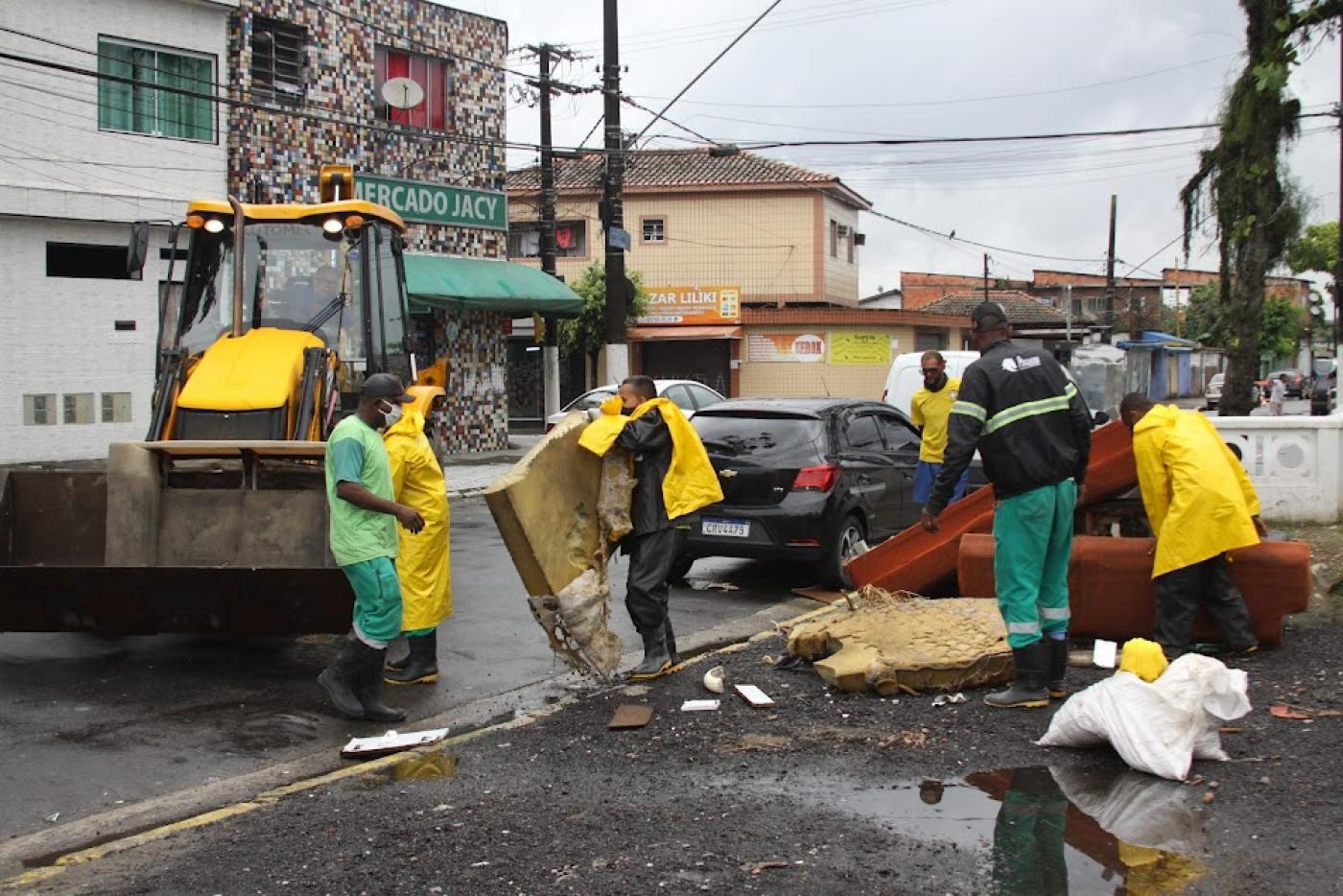funcionários recolhem colchão e móveis em área próximo a um canal. #paratodosverem