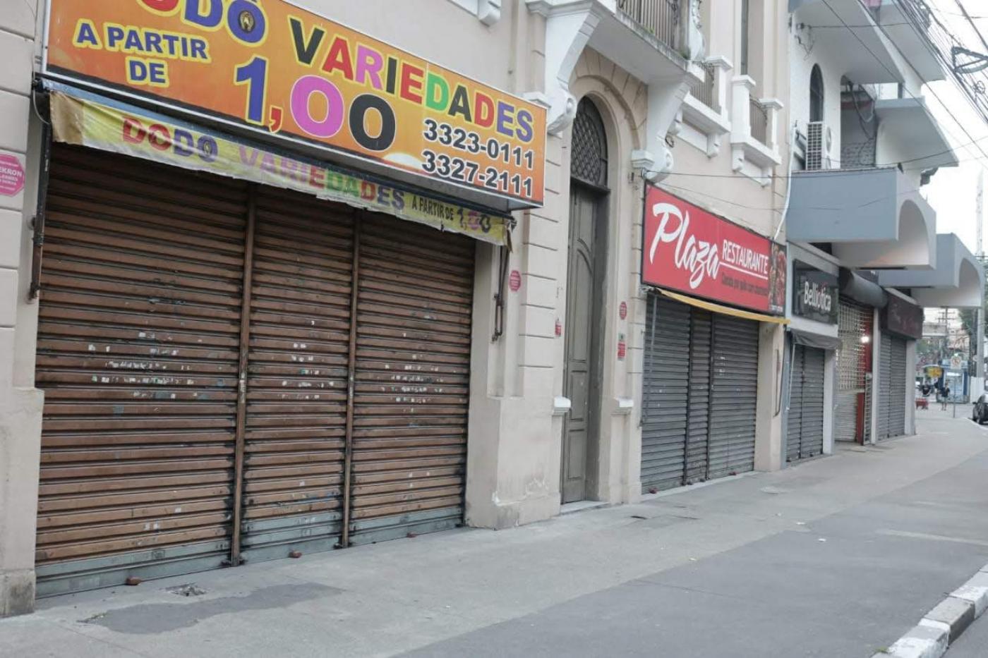 Várias lojas de rua com portas fechadas. Rua está vazia. #Paratodosverem