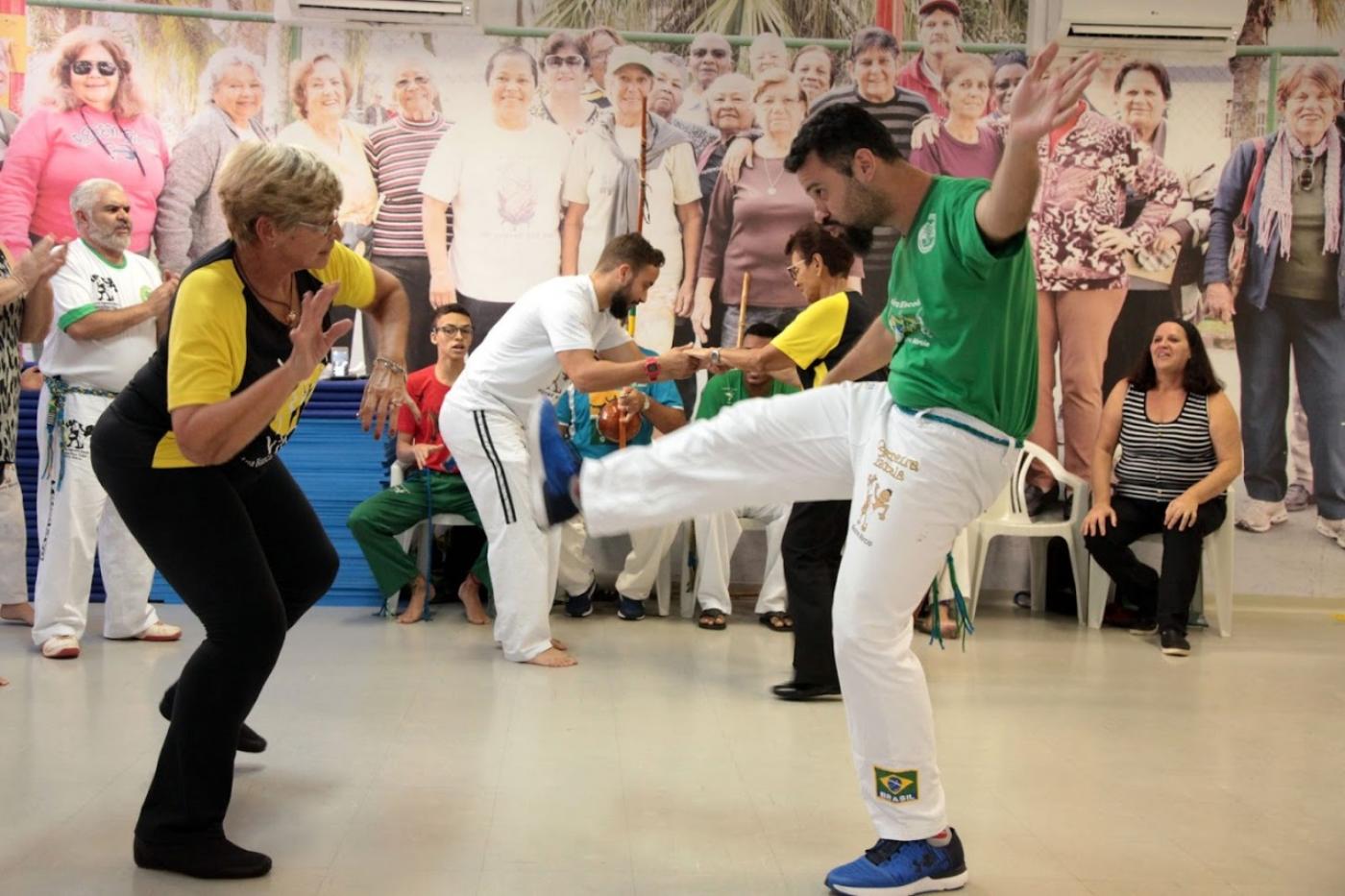 Um jovem e uma idosa praticam capoeira #paratodosverem