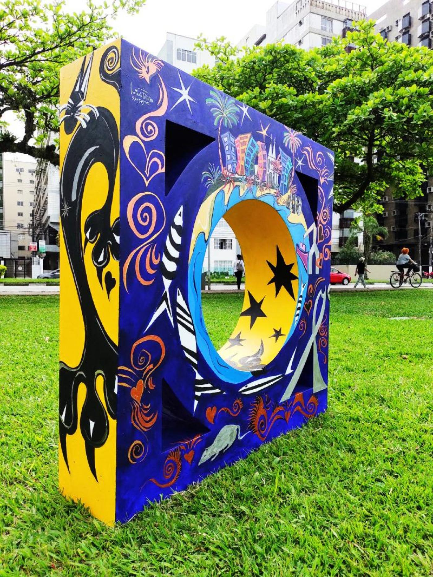 Escultura no jardim, em formato de mureta dos canais, colorida nas cores azul, amarelo e preto. #paratodosverem