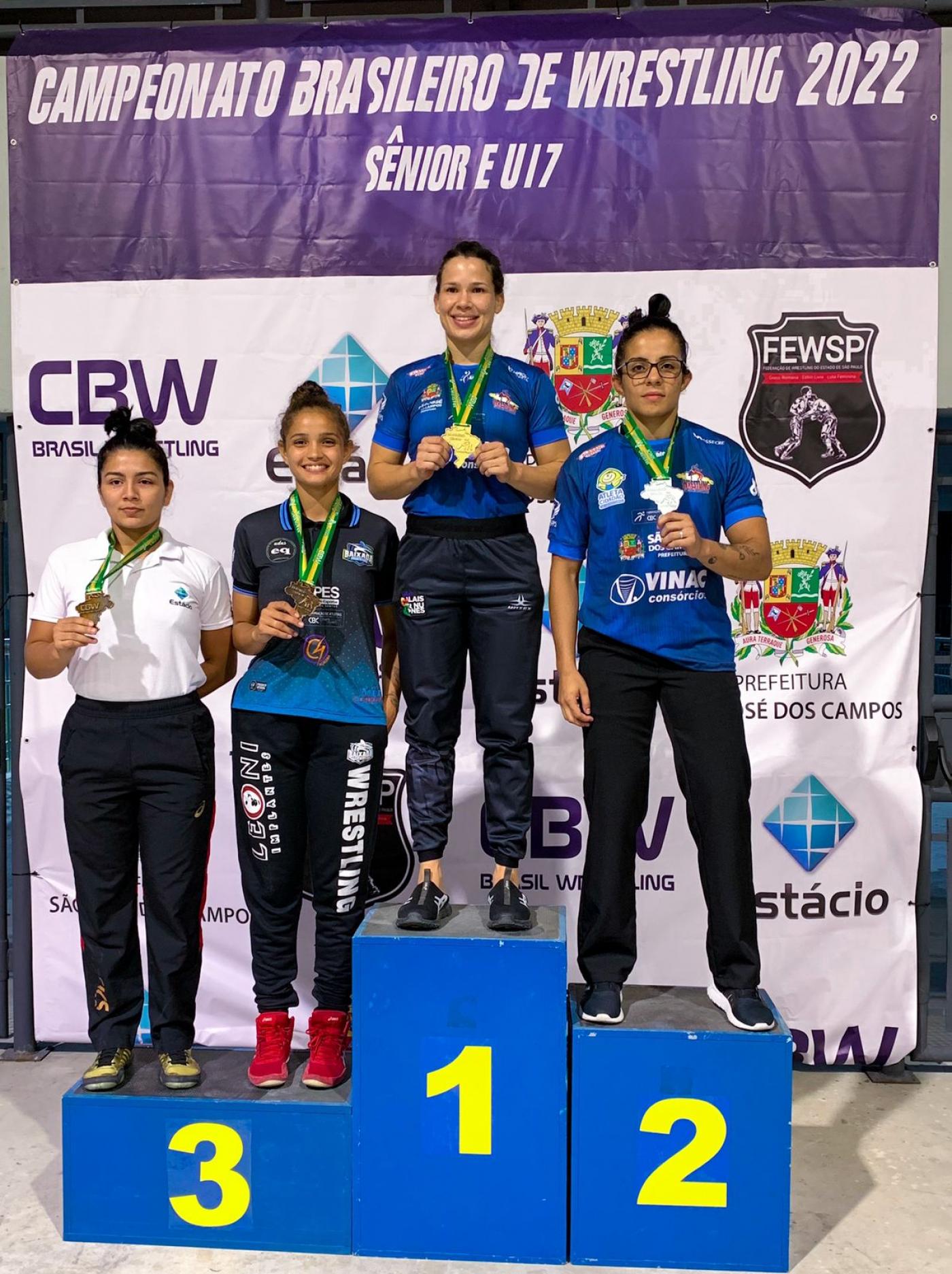 Pódio com as quatro primeiras colocadas segurando as medalhas penduradas em seus pescoços. #pratodosverem
