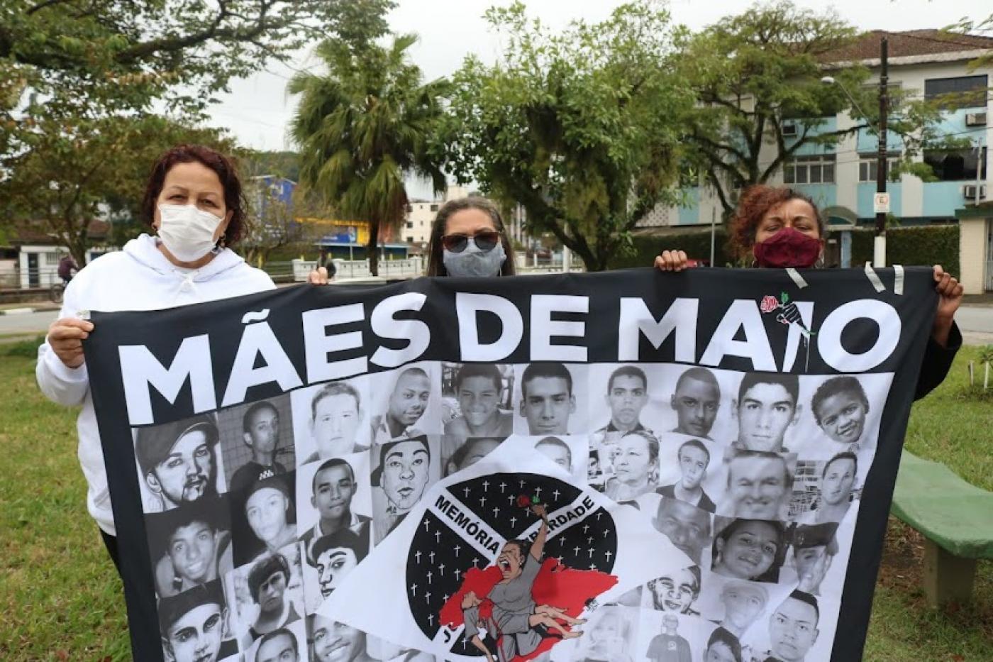 Mulheres mostram bandeira escrito mães de maio e com rostos de vitimas. #paratodosverem