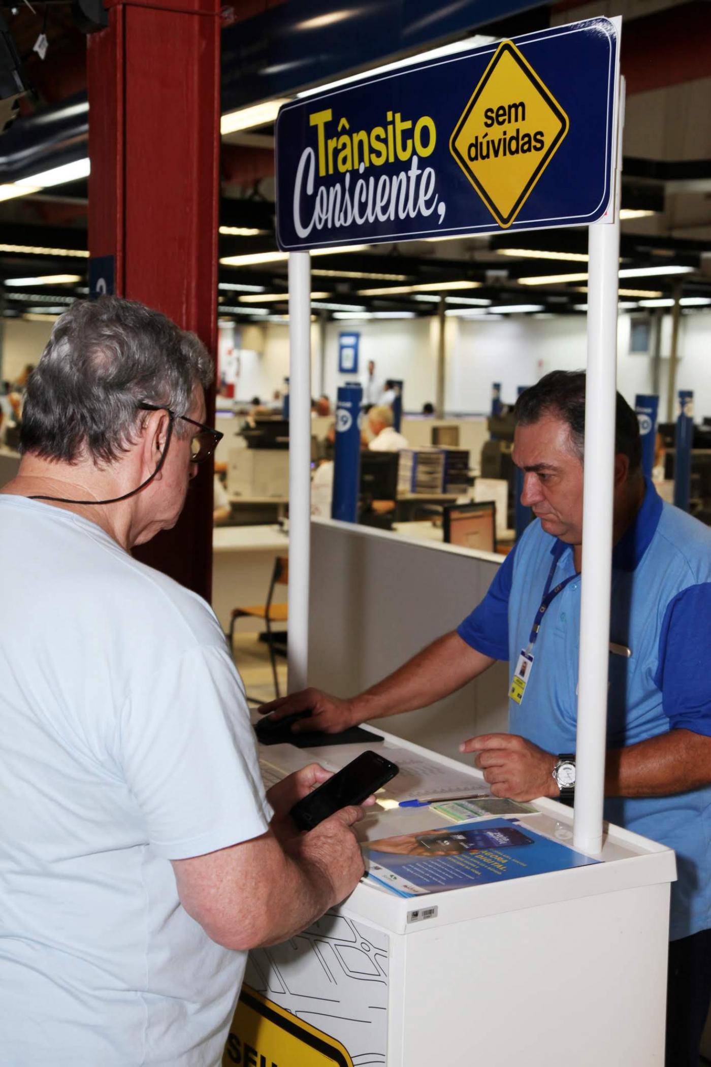 Estande da CET montado em uma área coberta. Um homem está pedindo informações ao outro que usa uniforme da empresa. #Pracegover