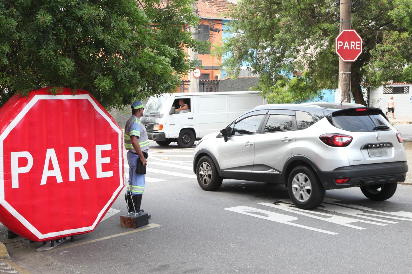 grande inflável onde se lê pare e agente de trânsito ao lado. Carros passam pela rua. #paratodosverem 