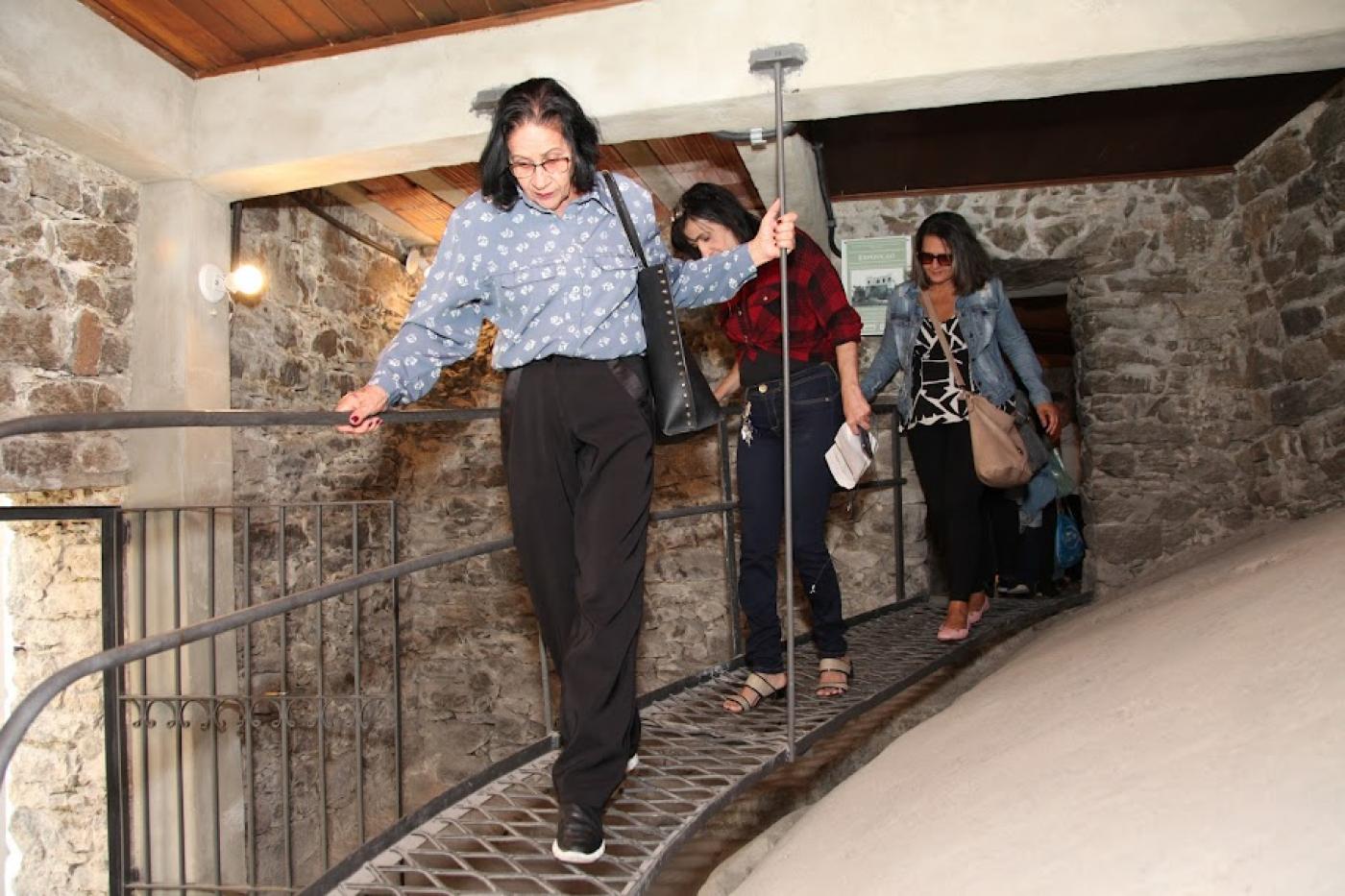 Três mulheres caminham em passsarela dentro de uma espécie de gruta. #paratodosverm 