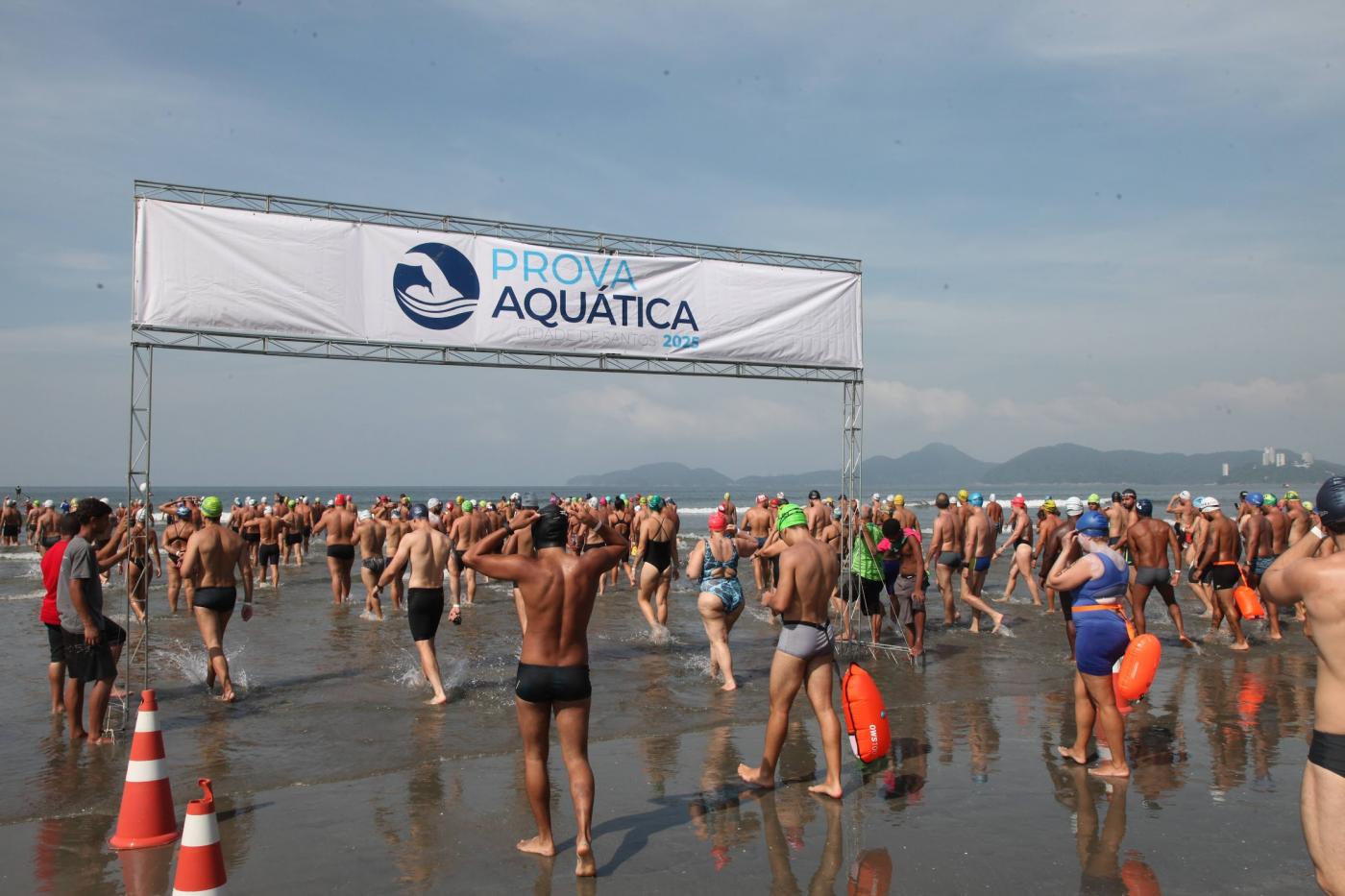 atletas entram no mar passando sob pórtico onde se lê prova aquática. #paratodosverem
