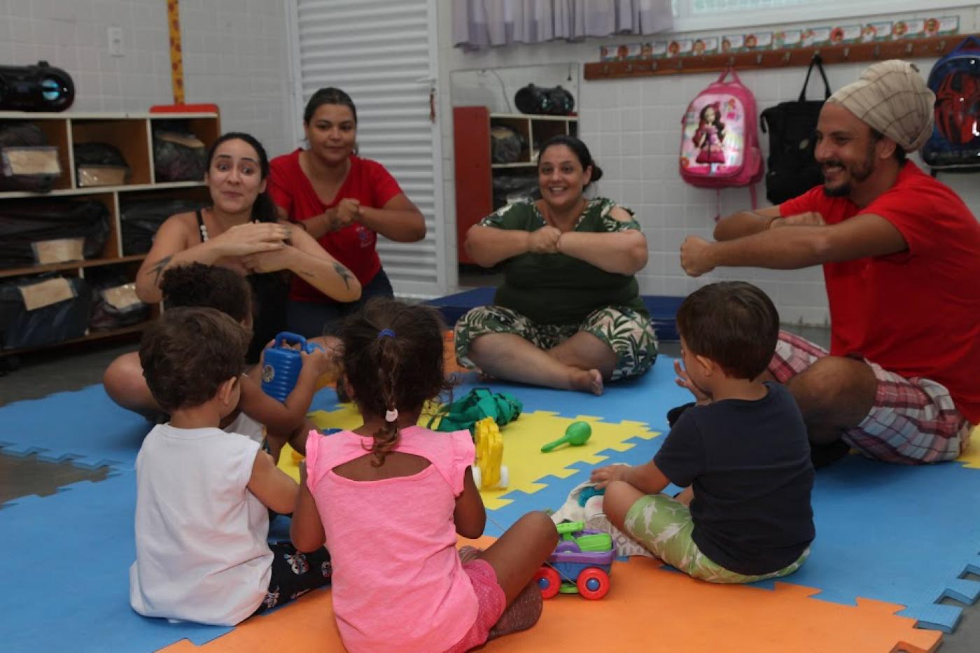 crianças e adultos estão sentados brincando e interagindo. #paratodosverem 