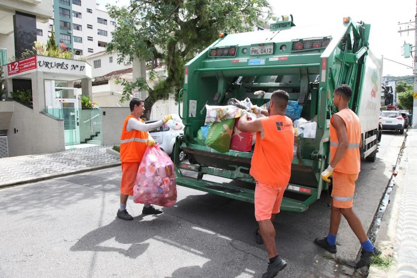 homens depositam sacos de lixo em caminhão. #paratodosverem 