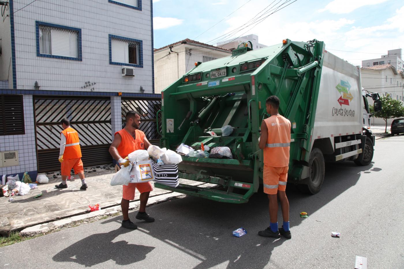 Coletores de lixo recolhem sacos em rua e os depositam em caminhão de coleta seletiva. #Pracegover
