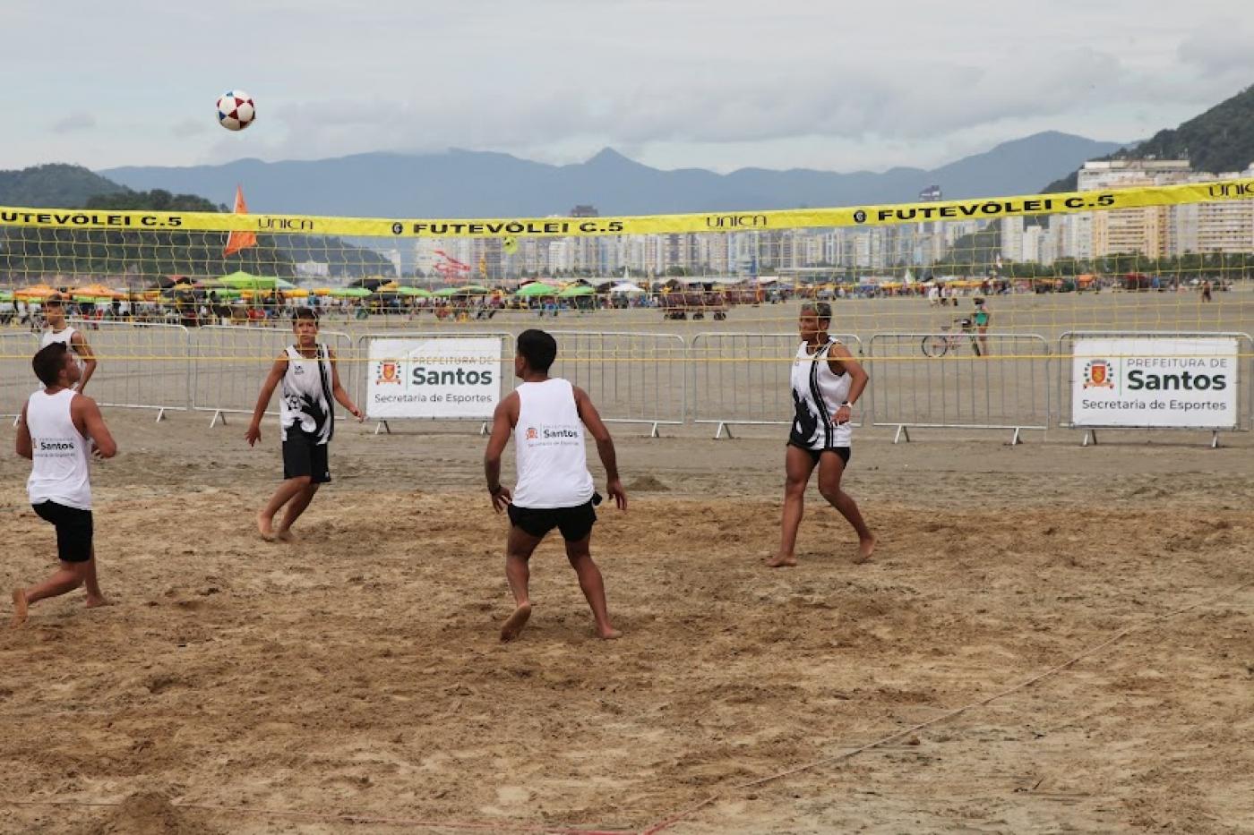 jogo de futevôlei nas areias da praia com dois atletas de cada lado da rede. #paratodosverem
