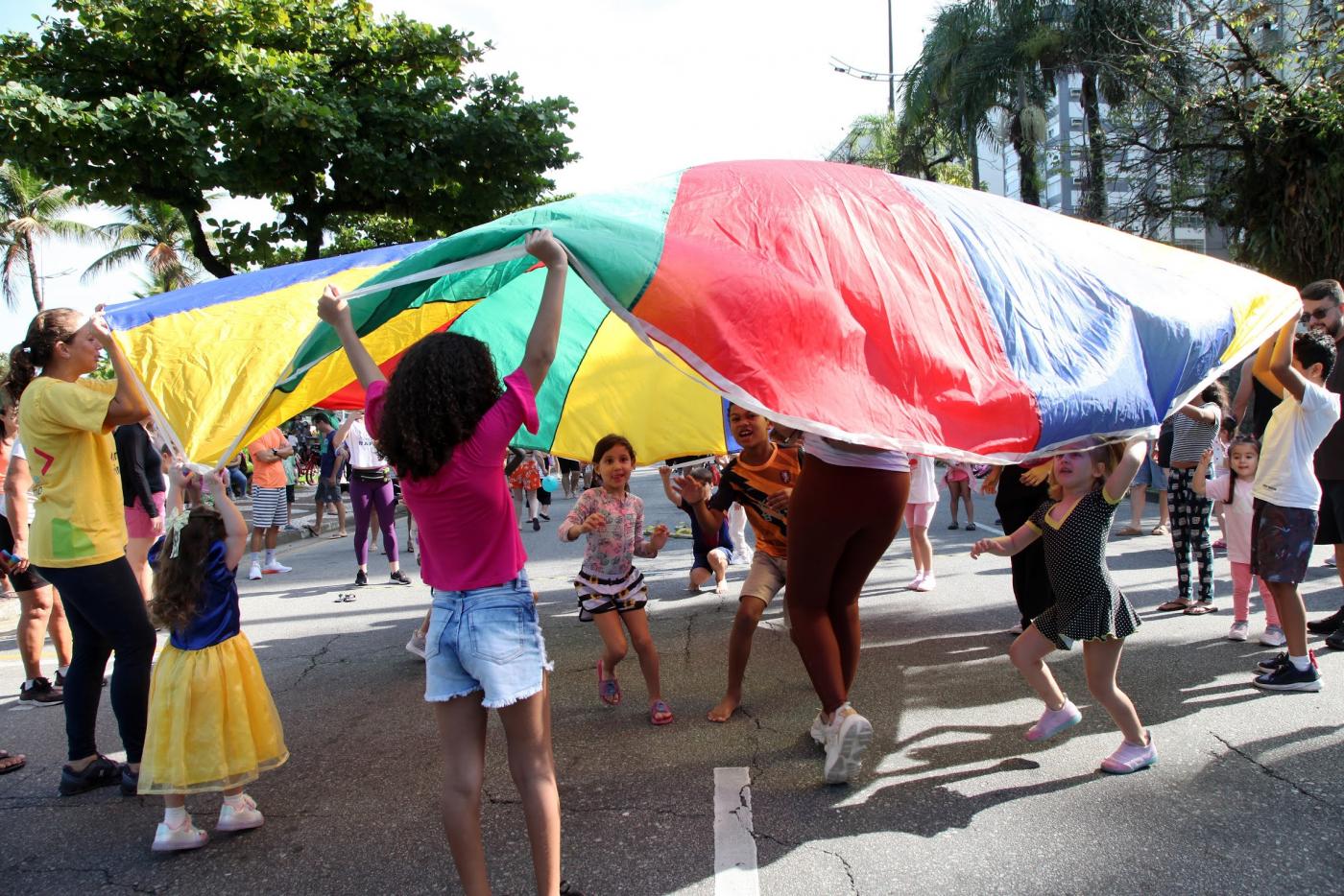 crianças brincam sob lona multicolorida. #paratodosverem