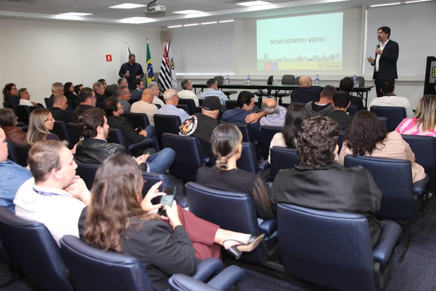 pessoas sentadas em auditório assistem palestra. #paratodosverem