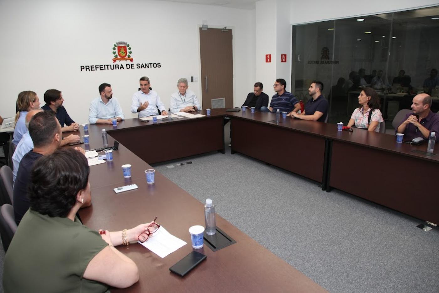várias pessoas sentadas em sala com mesas dispostas em formato de letra U. #paratodosverem