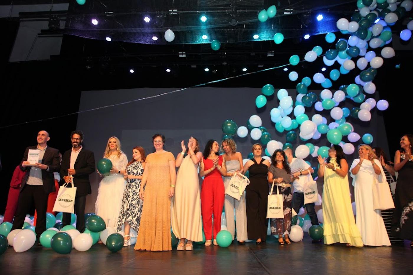 educadores premiados estão no palco. alguns aplaudem. Há balões de gás subindo. #paratodosverem 