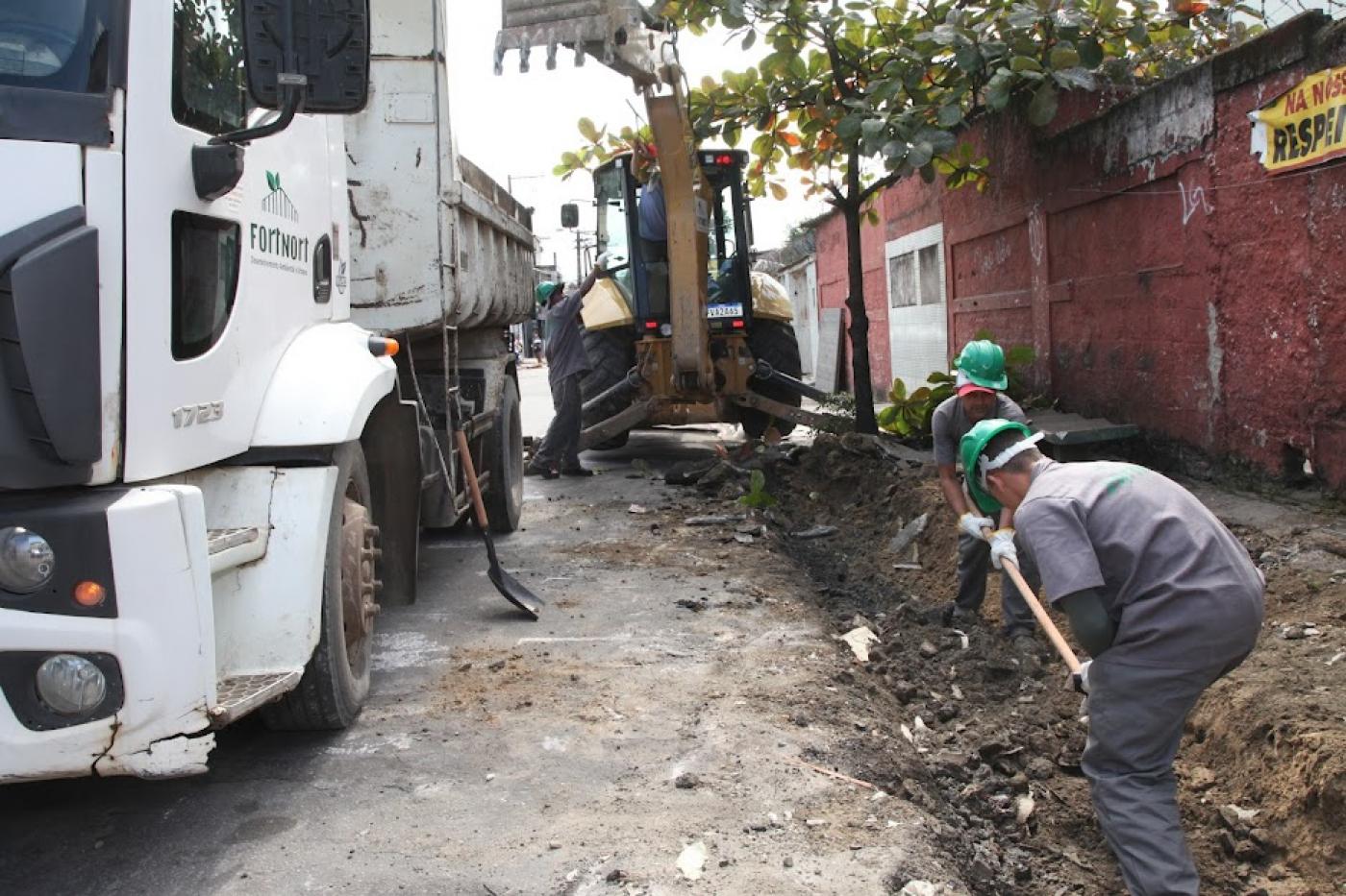 homens trabalhando em construção de sarjeta ao lado deum caminhão. #paratodosverem