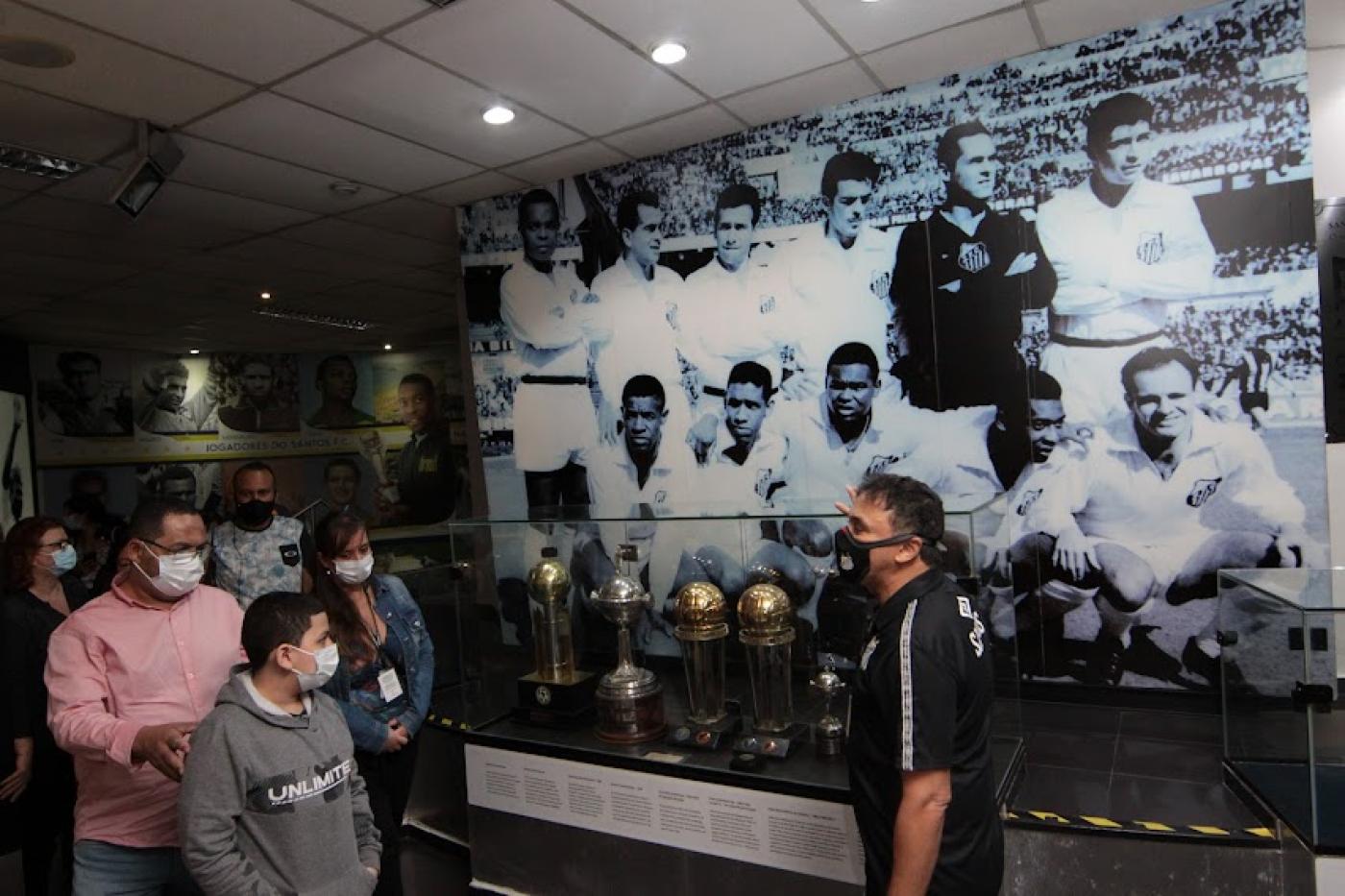 Homem mostra foto de time do Santos e troféus para visitantes #paratodosverem