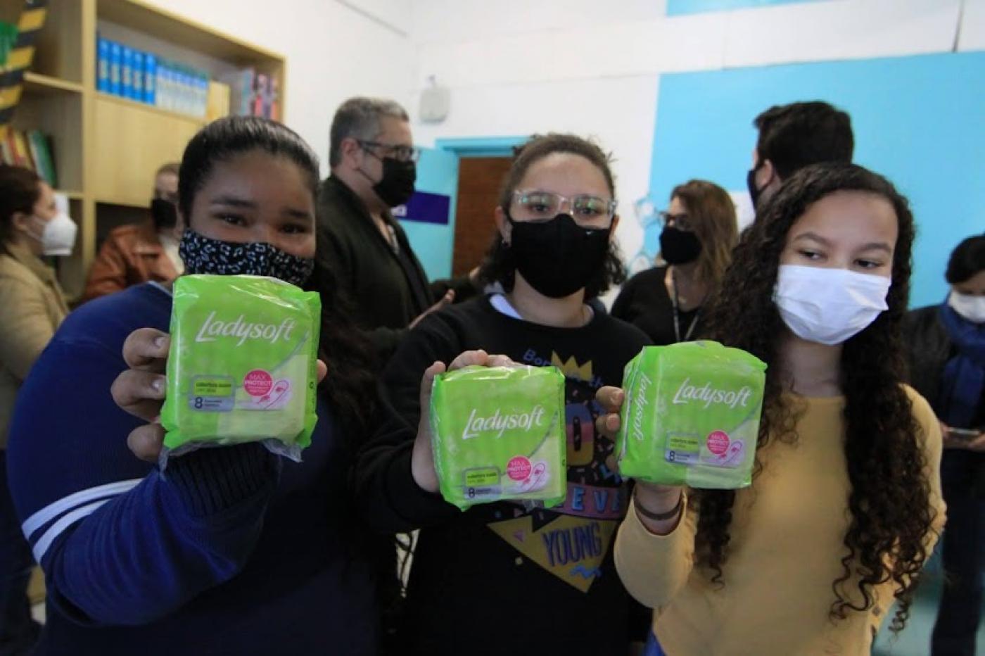 Meninas erguem pacote com absorvente #paratodosverem