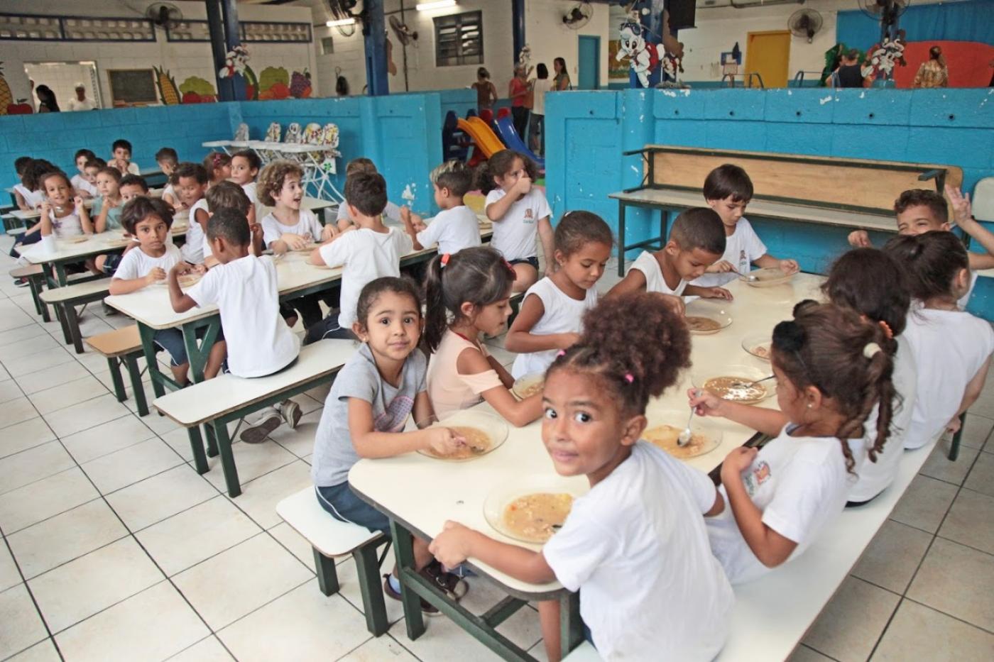 crianças sentadas comendo merenda escolar #paratodosverem