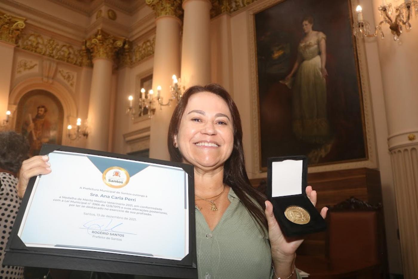 mulher segura diploma com a mão direita e medalha com a esquerda. #paratodosverem