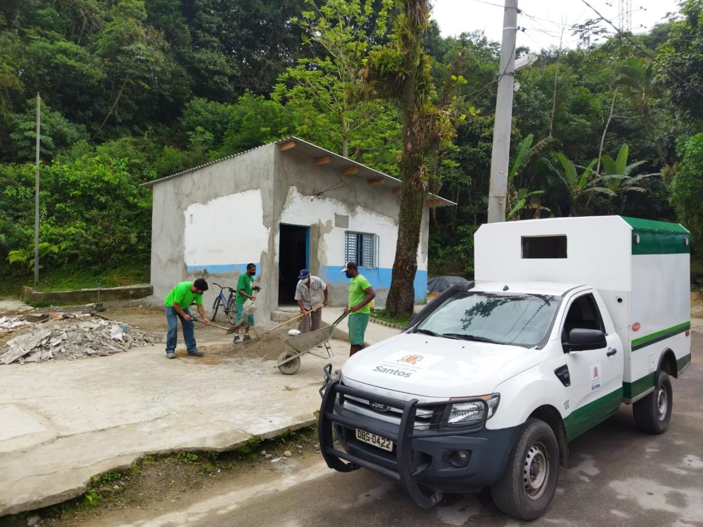 Homens trabalham em obra de prédio. Diante da calçada há um veículo da prefeitura estacionado. #paratodosverem