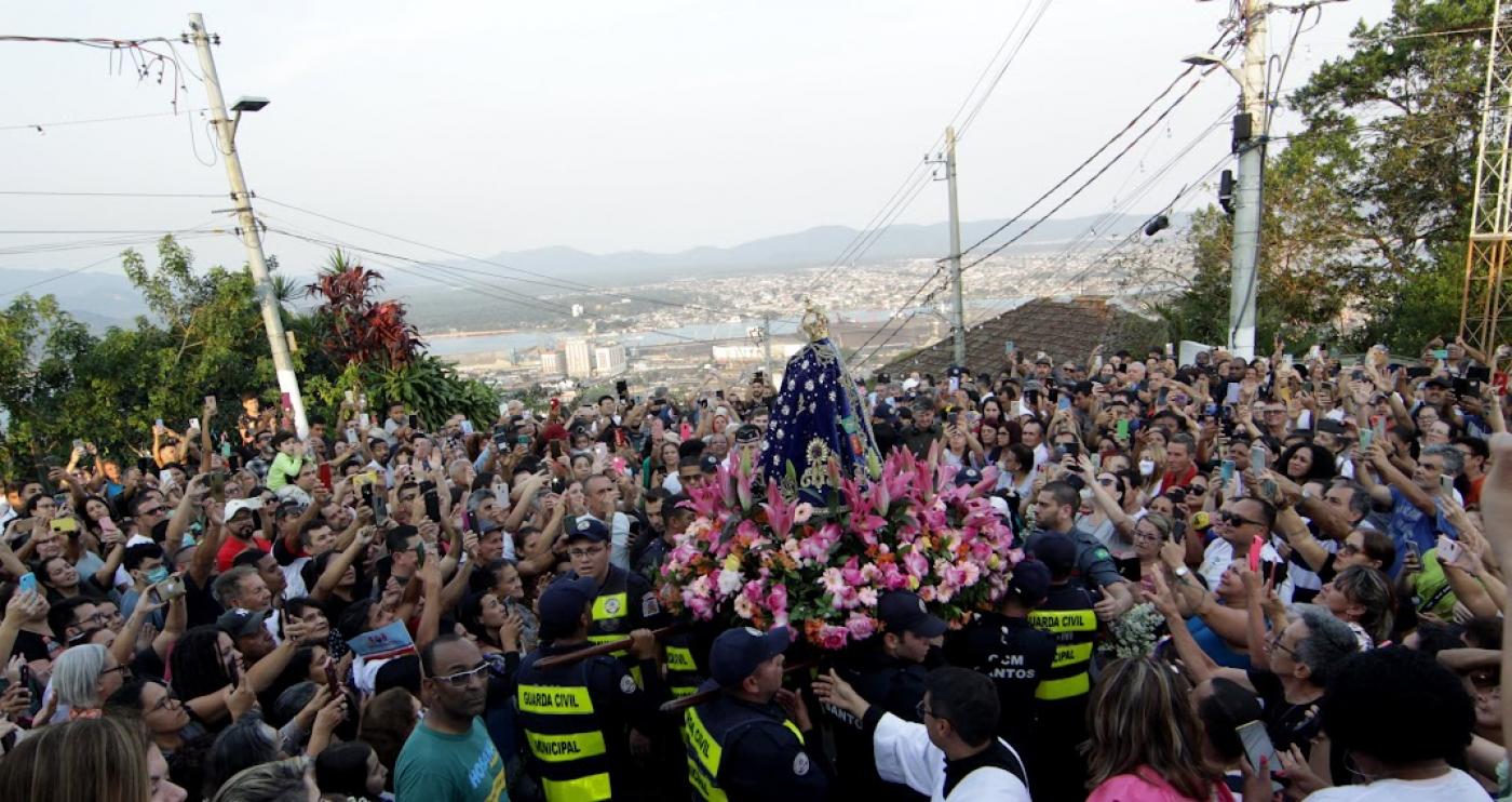 Imagem da Santa carregada por guardas municipais cercados por devotos no alto do Monte Serrat. #paratodosverem