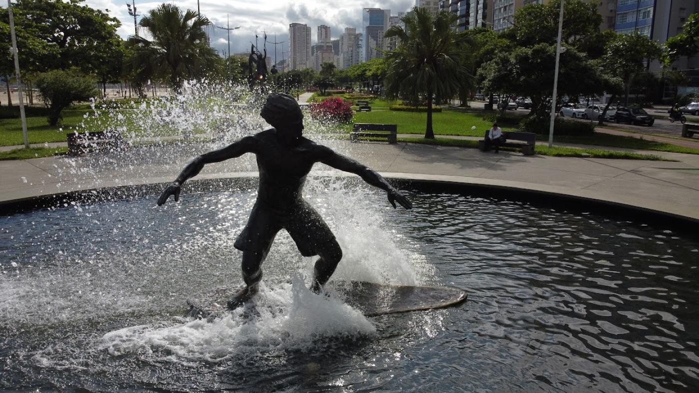 Escultura de homem sobre prancha com jatos de água e fonte no entorno. #paratodosverem