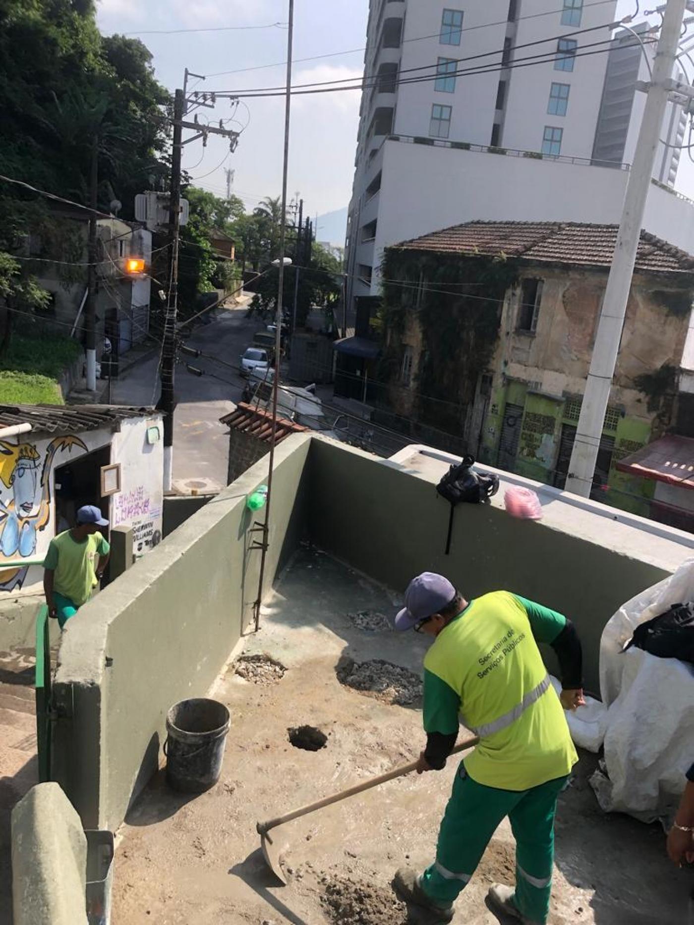 homem trabalha no piso com enxada. Espaço é na entrada de um morro. #paratodosverem