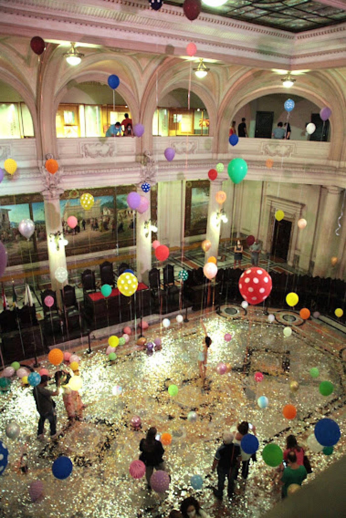 Balões ocupam do térreo ao teto do Museu do Café com público admirando.#pratodosverem