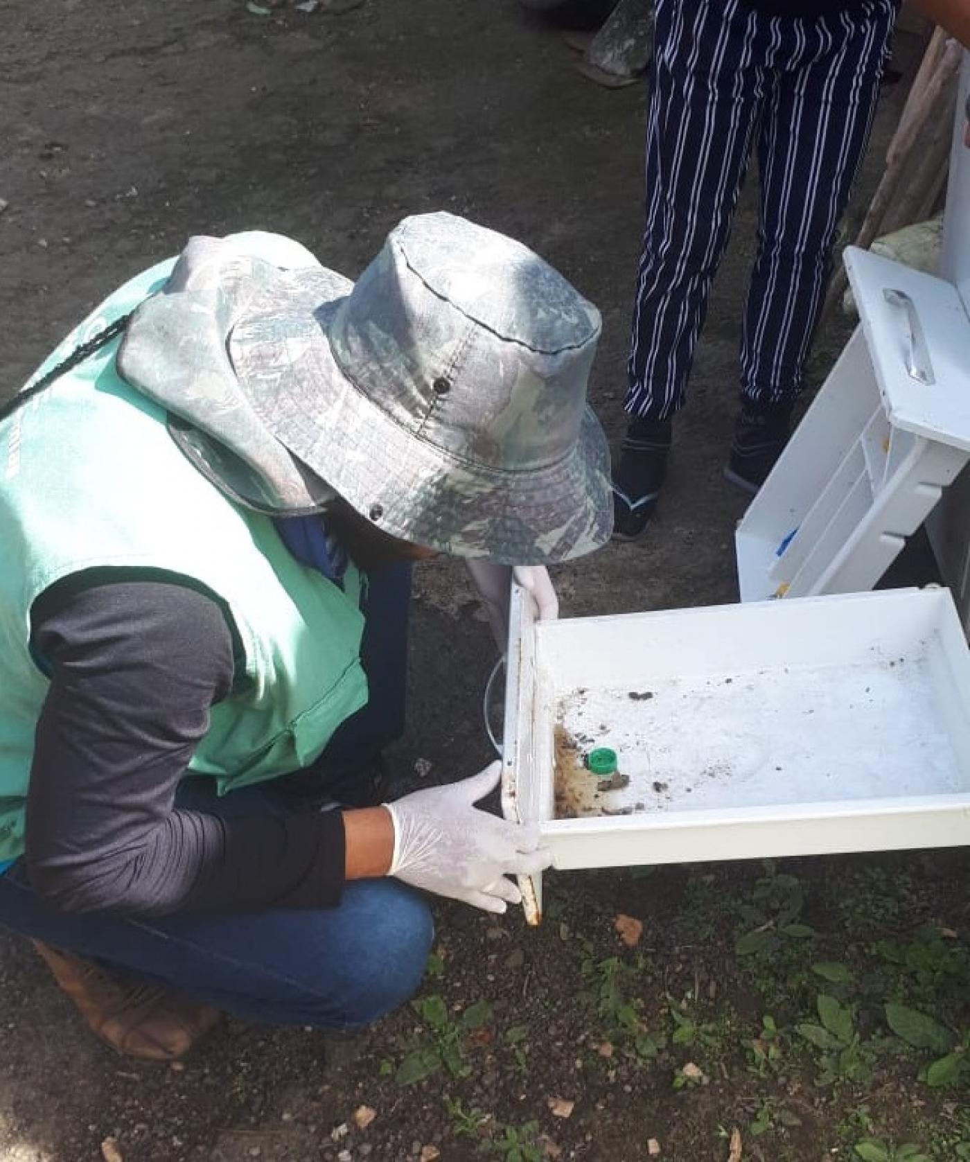 agente uniformizado e com chapéu abre gaveta em área aberta e gramada. #paratodosverem