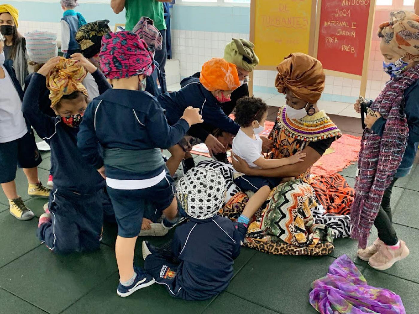 Mulher com turbante segurança criança no colo com várias ao redor usando turbantes #paratodosverem
