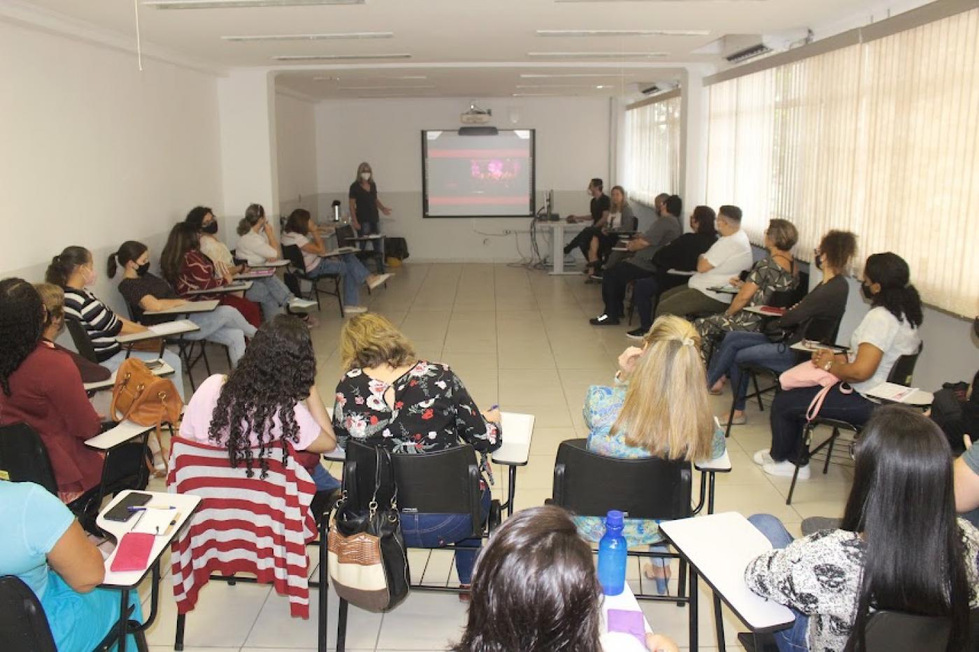 sala de aula com várias pessoas sentadas em roda assistindo a uma palestra. #paratodosverem