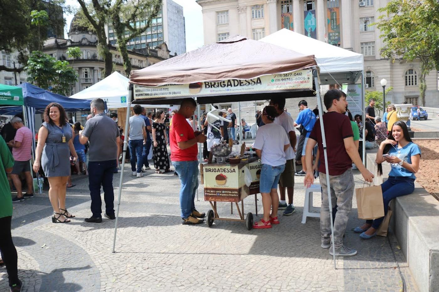 pessoas na praça com várias tendas #paratodosverem