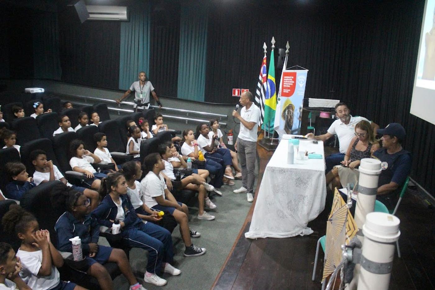 crianças estão sentadas em auditório assistindo palestra. #paratodosverem