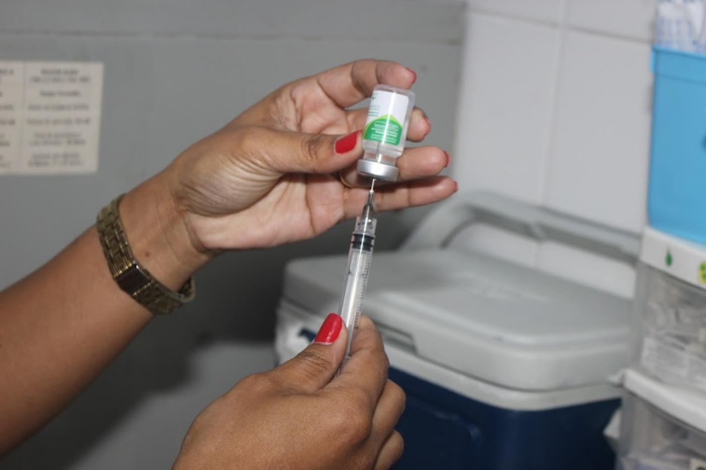 mãos seguram seringa enfiada em frasco de vacina. #paratodosverem