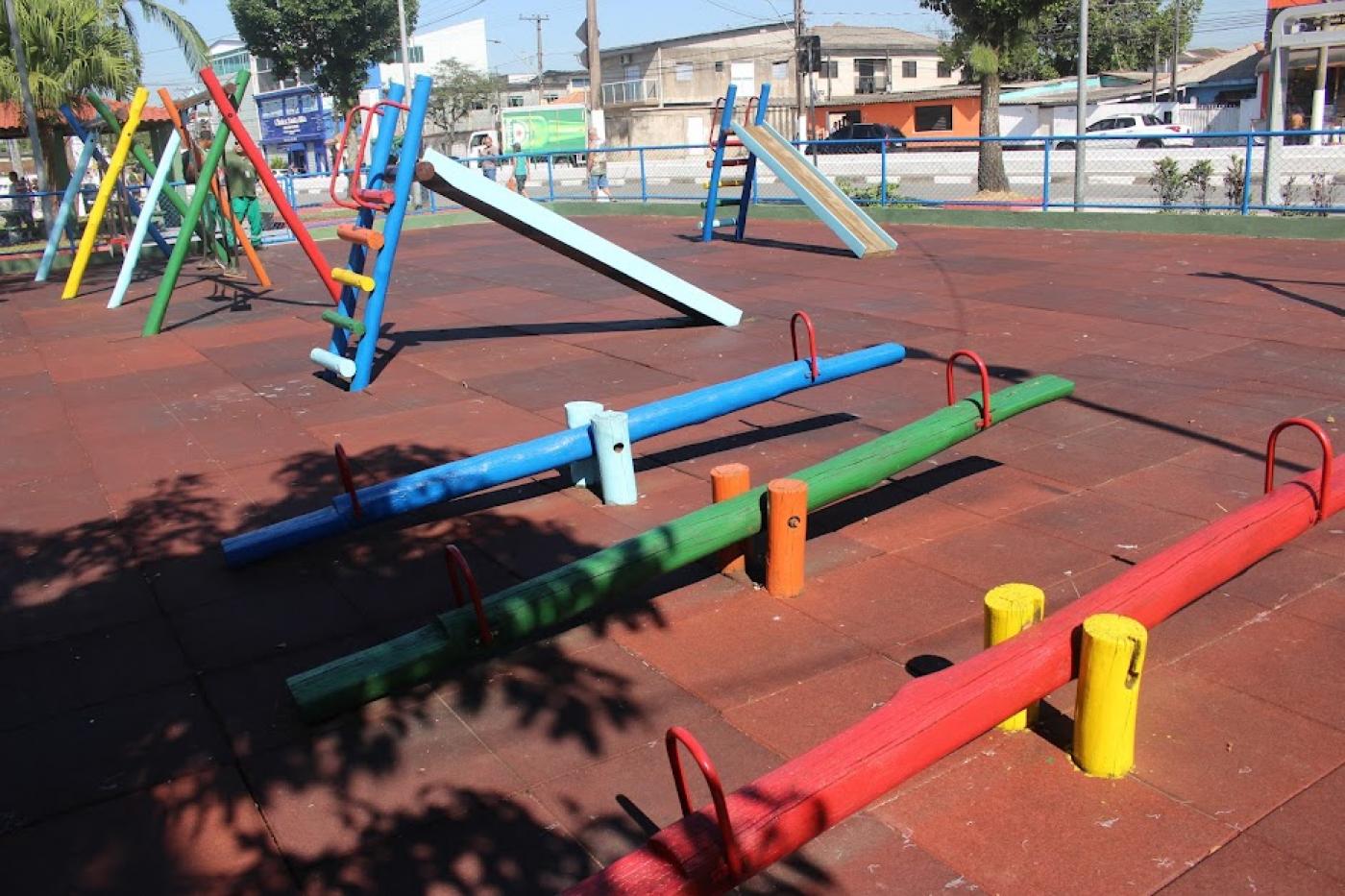 playground com gangorras em primeiro plano e escorregadores ao fundo. #paratodosverem 